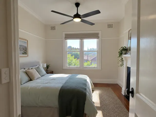 Ceiling fan in a light-filled bedroom with white walls, window and carpet in Cammeray