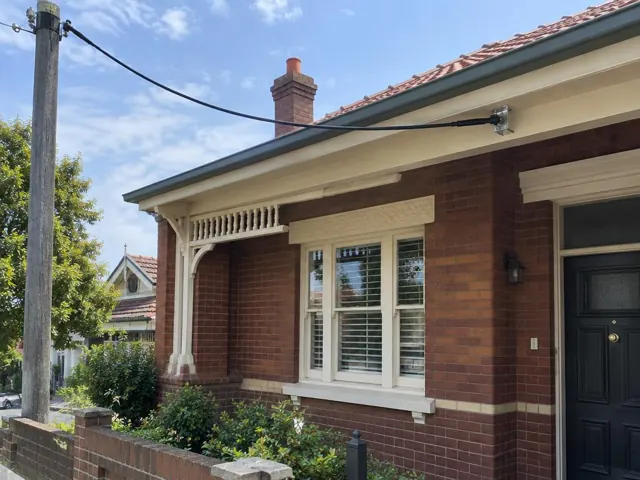 Brick house facade with overhead service cable and wall-mounted bracket near the eaves in Northbridge